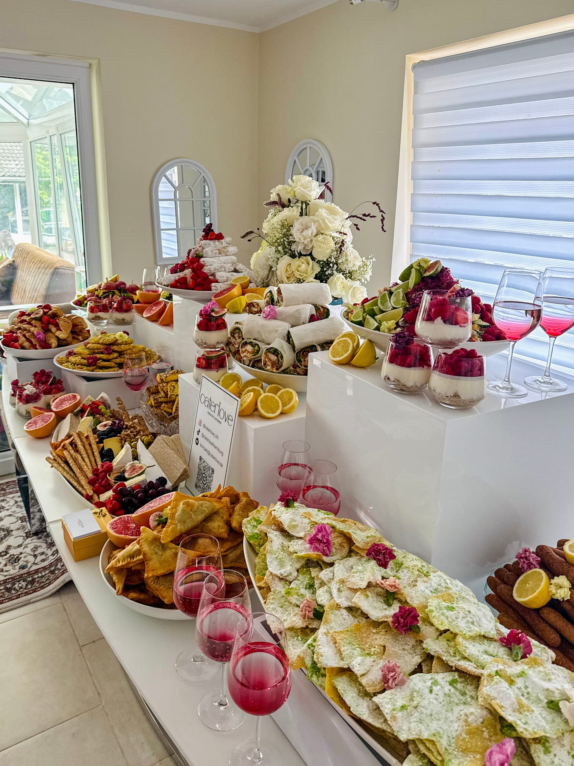 Süßes Buffet mit puderzuckerbestäubtem Gebäck, Rosenblüten, Dessertgläsern mit Himbeeren und pinken Getränken