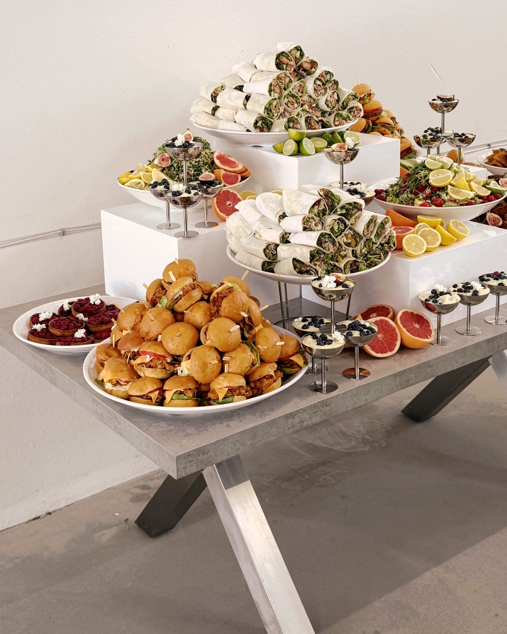 Buffettisch vor heller Wand: Wrap-Pyramide auf einem Sockel, Mini-Burger mit Käse und Tomate, Salat mit Feigen und Grapefruit